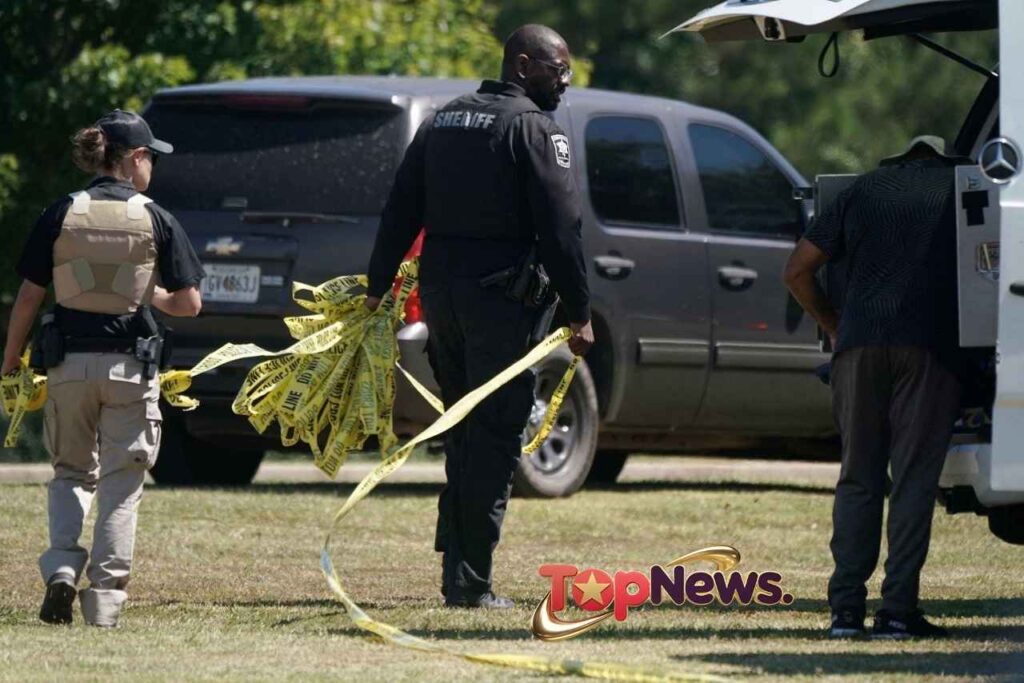 Law enforcement officers hold police tape near the scene.